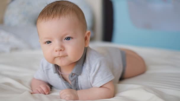 Un bambino mensile giace su un letto sul suo stomaco. Il ragazzo impara a tenere la testa. Un neonato giace sul suo stomaco in modo che i gas escano. Allevia le coliche . — Video Stock