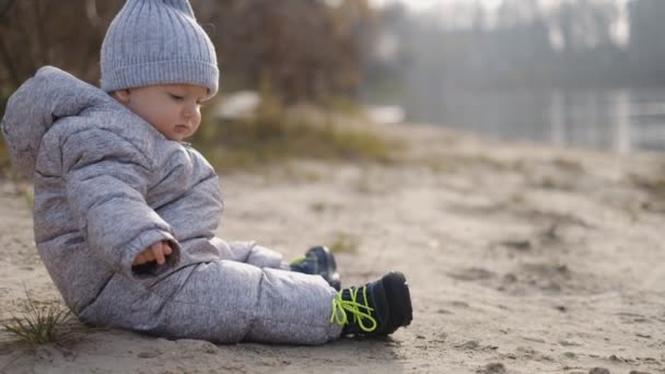 El chico se sienta en el río en primavera. Camina con un niño pequeño en la primavera cerca del río . — Vídeos de Stock