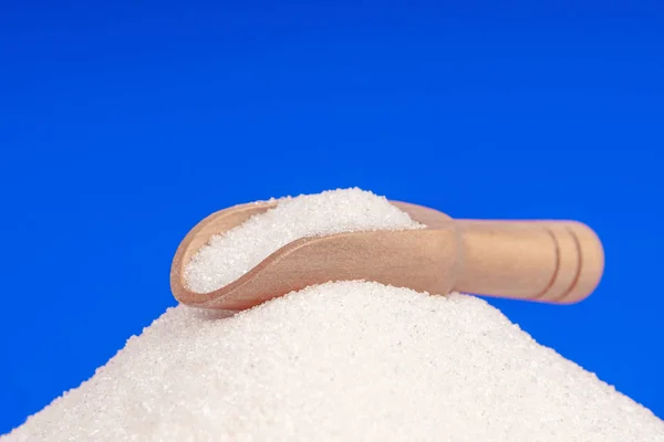 Mavi arka planda tahta kaşığı olan bir yığın beyaz şeker.