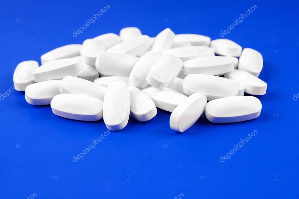 Heap of medical white pills on a blue background