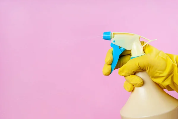 Gloved hand sprays out of a spray bottle on a pink background, copy space, mock up