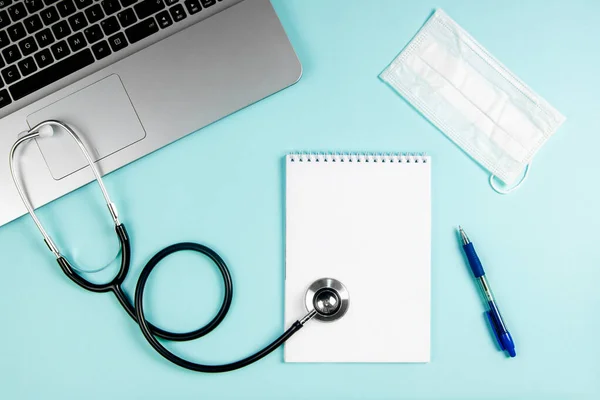 Dizüstü bilgisayarı, maskesi ve not defteri olan yassı bir doktor işyeri..