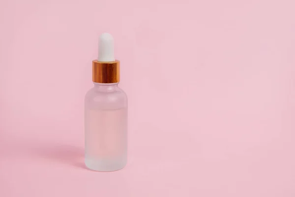 Pembe arka planda cam bir şişede yüz bakımı. Cilt bakımı kavramı.