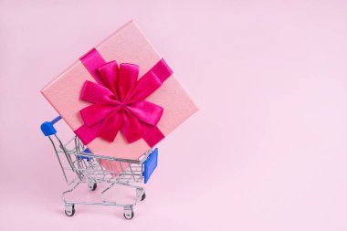 Pembe arka planda alışveriş arabasında harika bir hediye.