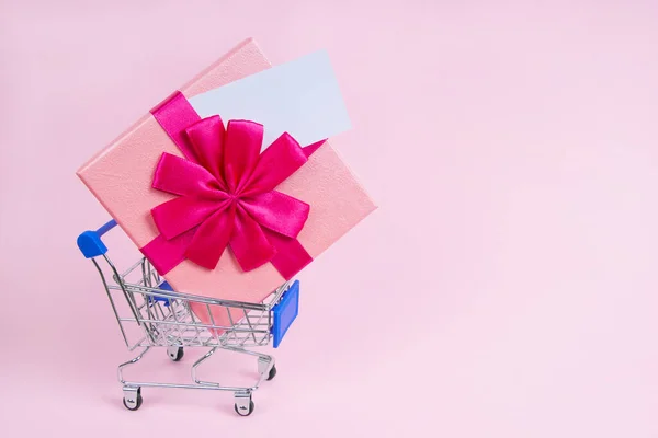 Alışveriş arabasında harika bir hediye, üzerinde de pembe bir arka plan var.