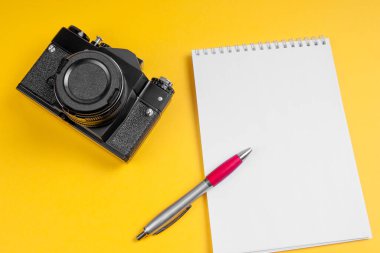 Kamera ve sarı arka planda kalem olan defter. Model-up. Fotoğraf konsepti.