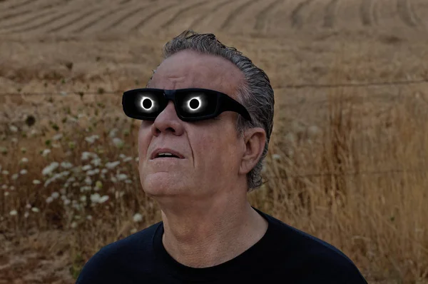 Man looking at full solar eclipse with eclipse reflecting in lenses of glasses