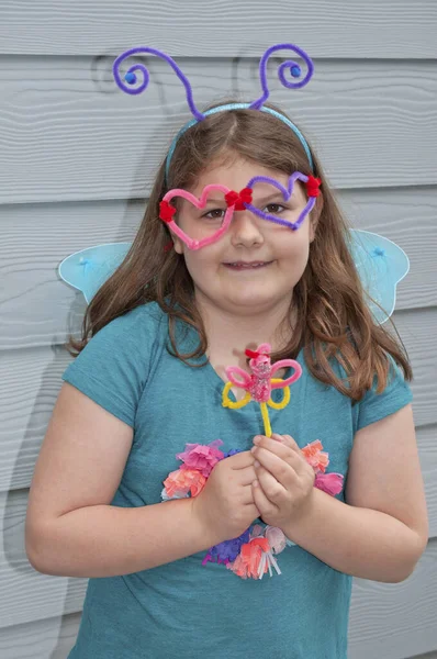 Girl with pipe cleaner craft projects of a butterfly and glasses. Stay at home crafting.