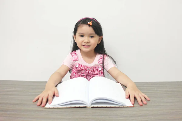Söpö hymyilevä pieni aasialainen tyttö kirjan kanssa — kuvapankkivalokuva