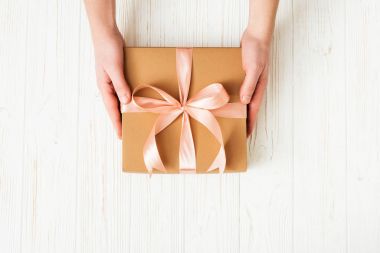 Adam beyaz ahşap zemin üzerinde pembe fiyonklu hediye kutusu tutan eller