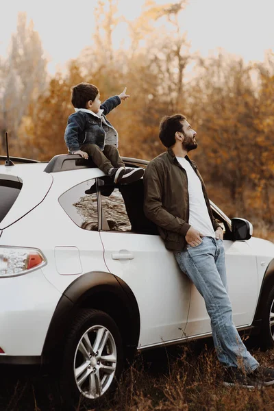 Pai feliz empilhando perto do carro com seu filho sentado no carro e apontando para o céu . — Fotografia de Stock