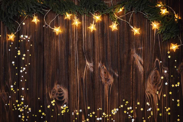Christmas garland lights, golden stars and fir branches on wooden rustic background. — Stock Photo, Image