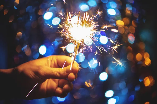 Mão segurando um fogo de artifício sparkler queima no fundo bokeh luz de Natal . — Fotografia de Stock