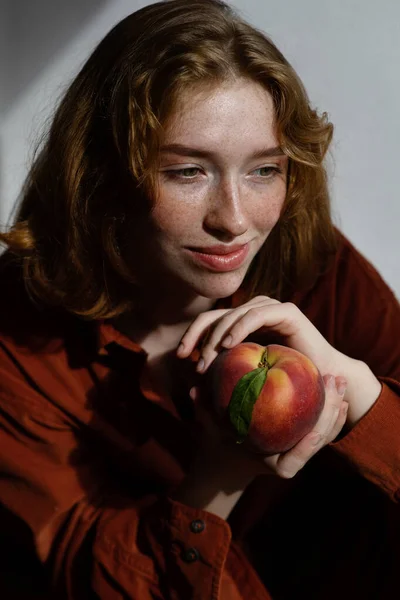 Retrato de mulher sorridente com longos cabelos vermelhos segurando pêssego maduro . — Fotografia de Stock