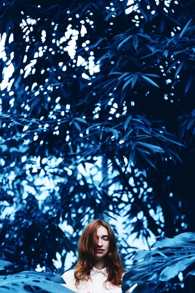 Beautiful redhead woman in tropical garden toned in blue. — Stock Photo, Image