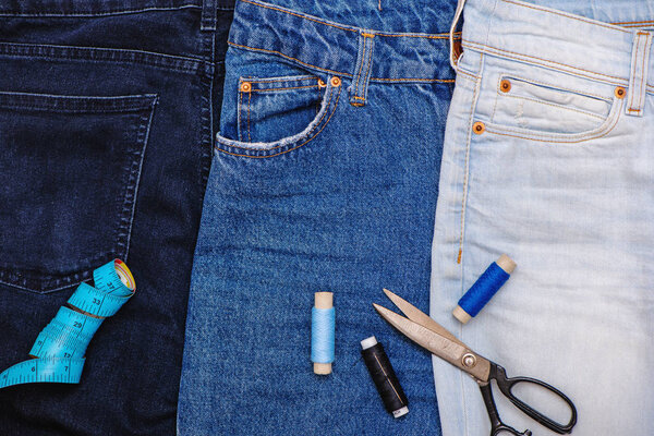 Three pair of jeans with scissors, threads and tailor meter.