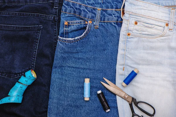 Three pair of jeans with scissors, threads and tailor meter. Stock Photo