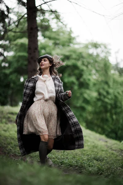 Mulher bonita em boné de pico e casaco xadrez correndo na floresta . — Fotografia de Stock