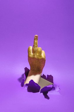 Orta parmağıyla menekşe arkaplanındaki kağıt delikten el hareketi yapan bir adam..