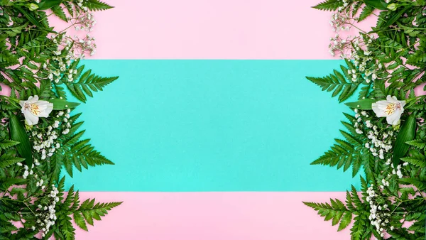 Yeşil eğreltiotu yapraklarından yapılmış bahar bayrağı ve pembe ve turkuaz arka planda beyaz çiçekler.