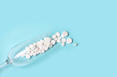 Mavi arka planda boş şarap kadehinde ilaç..