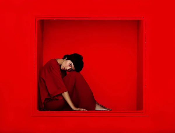 Colpo di moda di giovane bella donna seduta in nicchia su sfondo rosso . — Foto Stock