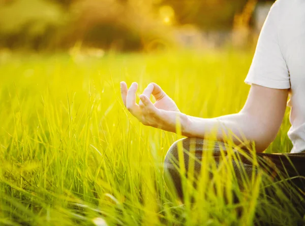 O homem está meditando na grama verde no parque no dia ensolarado de verão. Conceito de meditação e estilo de vida saudável — Fotografia de Stock