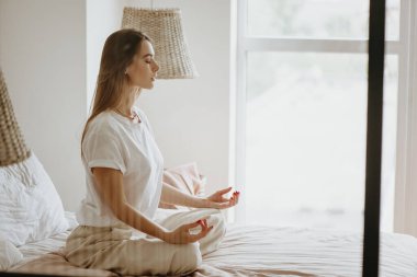 Genç kadın yatakta meditasyon yapıyor..