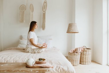 Genç kadın yatakta meditasyon yapıyor..