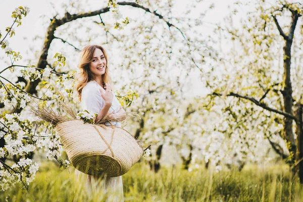 Vrouw met rieten zak in het voorjaar appel bloesem. — Stockfoto