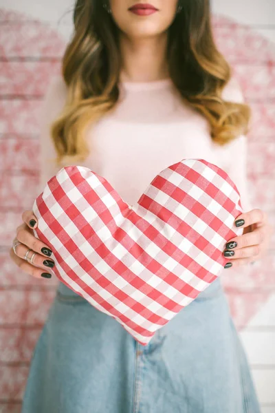 Joven hermosa mujer sostiene almohada en forma de corazón en stu decorado —  Fotos de Stock