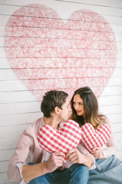 Unga par med hjärtformade kuddar poserar för kärlekshistoria i — Stockfoto