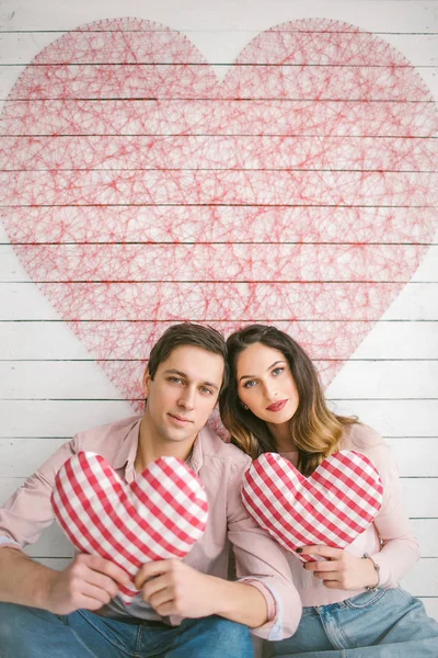 Unga par med hjärtformade kuddar poserar för kärlekshistoria i — Stockfoto