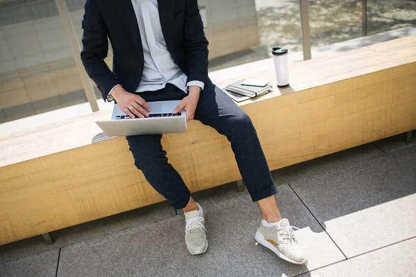 Joven hombre de negocios hipster en traje de escribir portátil cerca de la oficina outd —  Fotos de Stock