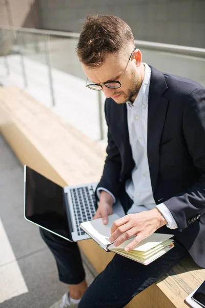 Jovem homem de negócios hipster em terno digitando laptop perto de escritório outd — Fotografia de Stock