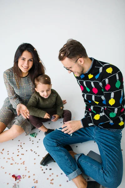 Giovane coppia con figlio che festeggia con coriandoli su sfondo bianco — Foto Stock