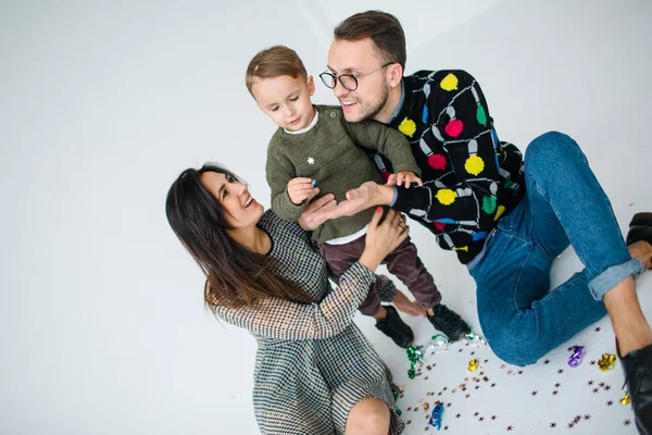 Giovane coppia con figlio che festeggia con coriandoli su sfondo bianco — Foto Stock