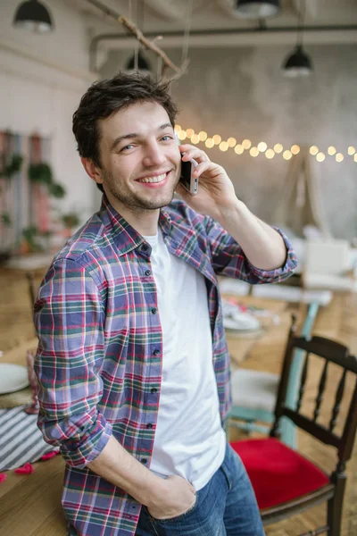 Joven hombre con camisa a cuadros con smartphone en loft rústico — Foto de Stock