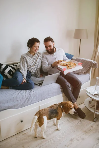 Joven pareja hipster casa comer pizza con portátil y perro — Foto de Stock