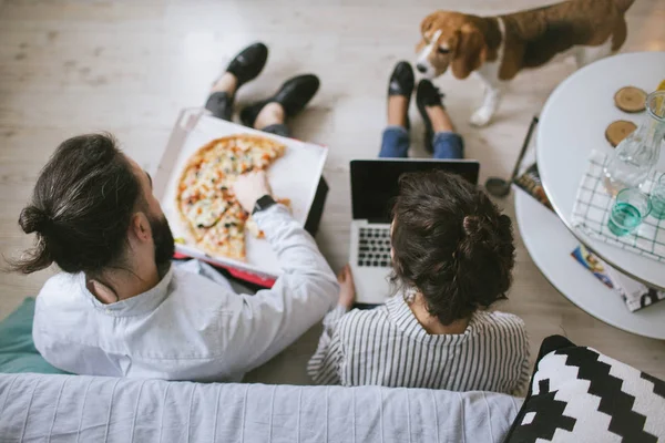 Genç hippi çift ev dizüstü bilgisayar ve köpek pizza yemek
