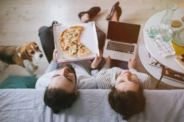 Genç hippi çift ev dizüstü bilgisayar ve köpek pizza yemek — Stok fotoğraf