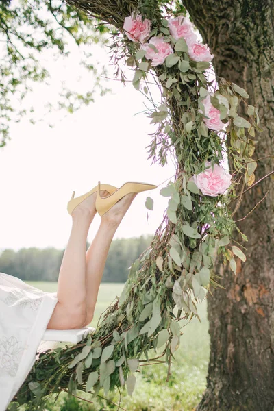 Mooie vrouw in witte jurk op schommel buitenshuis met bloemen — Stockfoto