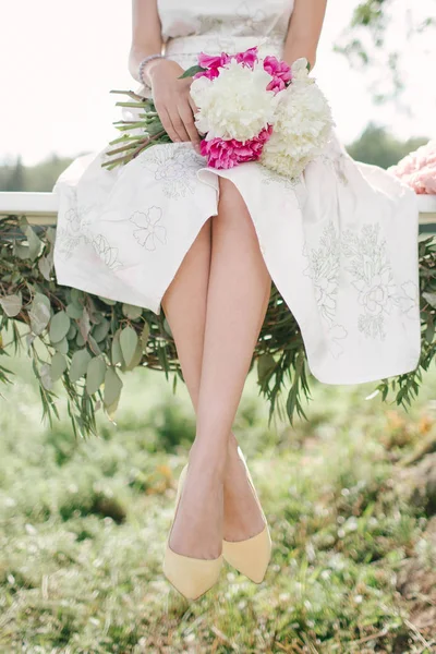 Όμορφη γυναίκα στην Λευκή φόρεμα σε κούνια σε εξωτερικούς χώρους με λουλούδια — Φωτογραφία Αρχείου