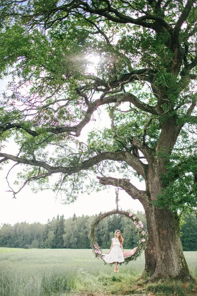 Hermosa mujer en vestido blanco en swing al aire libre con flores —  Fotos de Stock