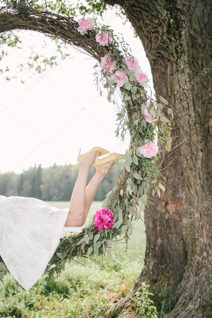 Beautiful woman in white dress on swing outdoors with flowers