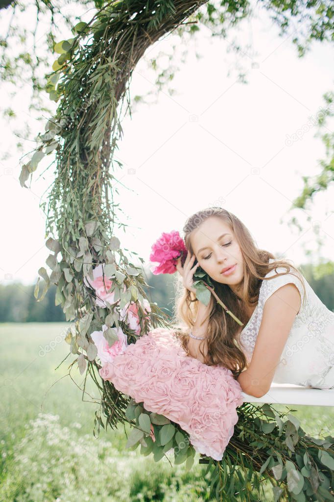 Beautiful woman in white dress on swing outdoors with flowers