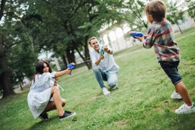 Parkta genç anne su silahlarla oynayan erkek bebek