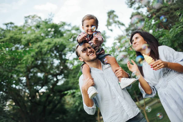 屋外の公園でバブル ワンドで遊んで幸せな若い家族 — ストック写真