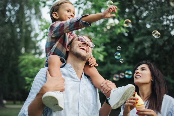 Feliz joven familia jugando con varitas de burbujas en el parque al aire libre — Foto de Stock