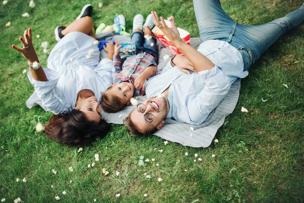 若い母親は、父男の子の屋外の芝生の上を敷設 — ストック写真